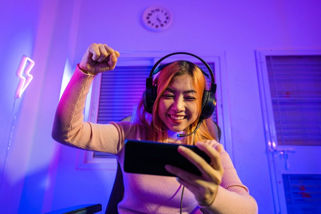 Une femme souriante joue sur un smartphone avec un casque de jeu.