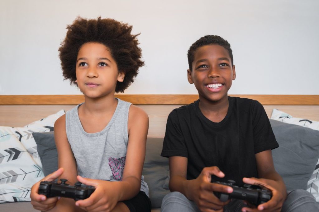 Deux garçons souriants jouant aux jeux vidéo sur un canapé.